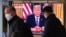 Masked people walk in front of a TV screen showing a live broadcast of U.S. President Donald Trump's speech at the Seoul Railway Station in Seoul, South Korea, March 12, 2020. 