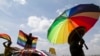 FILE - A person holds an umbrella bearing the colors of the rainbow flag as others wave flags during a gay pride rally in Entebbe, Uganda, Aug. 9, 2014. A crowd in Ghana tore down a billboard promoting LGBTQ tolerance in June 2022, during Pride month.