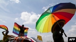 FILE - A person holds an umbrella bearing the colors of the rainbow flag as others wave flags during a gay pride rally in Entebbe, Uganda, Aug. 9, 2014. A crowd in Ghana tore down a billboard promoting LGBTQ tolerance in June 2022, during Pride month.