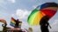 FILE - A person holds an umbrella bearing the colors of the rainbow flag as others wave flags during a gay pride rally in Entebbe, Uganda, Aug. 9, 2014. 