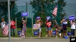 FILE - Supporters hold signs as Republican presidential nominee former President Donald Trump passes in a motorcade en route to a stop at a campaign office in Roseville, Michigan. Aug. 26, 2024.