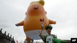 A woman posing as statue of liberty stands next to the 'Trump Baby' blimp as people gather to demonstrate against the state visit of President Donald Trump in Parliament Square, central London, June 4, 2019.