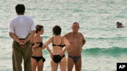 A fully clothed man enjoys the view as he walks along the beach, as two women talk to a man on the Umm Suqaim public beach in Dubai, United Arab Emirates, Monday, July 16, 2008. Authorities in the Persian Gulf tourist haven of Dubai are cracking…