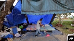 FILE - A resident sweeps at a camp set up on the shore of Laguna de Condado in San Juan, Puerto Rico, Oct. 23, 2017.