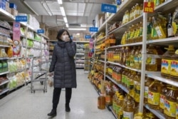 A shopper wearing a face mask browses an aisle of cooking oil in a supermarket in Beijing on March 16, 2020.