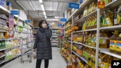 A shopper wearing a face mask browses an aisle of cooking oil in a supermarket in Beijing on March 16, 2020. 