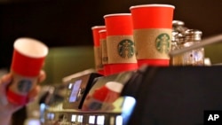 A barista reaches for a red paper cup as more, with cardboard liners already attached, line the top of an espresso machine at a Starbucks coffee shop in the Pike Place Market in Seattle, Nov. 10, 2015.
