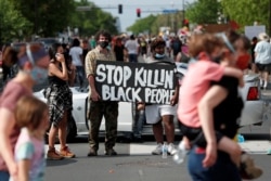 FILE - Protesters gather at the scene where George Floyd, an unarmed black man, was pinned down by a police officer kneeling on his neck before later dying in a hospital in Minneapolis, Minnesota, May 26, 2020.