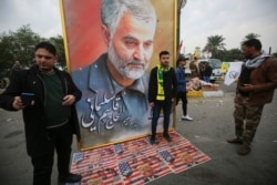 FILE - Supporters of the Hashed al-Shaabi paramilitary force and Iraq's Hezbollah brigades pose for a picture next to a poster of Iranian Quds Force commander Qassem Soleimani, in Baghdad, Iraq, Jan. 4, 2020