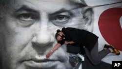 A woman takes part in a protest against Israeli Prime Minister Benjamin Netanyahu, seen on the poster, in Tel Aviv, Israel, April 19, 2020.