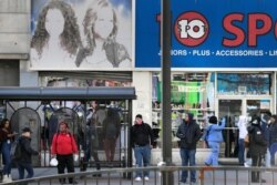 Pedestrians stand near a bus stop at an intersection in Newark, N.J., March 26, 2020. Police departments are taking a lead role in enforcing social distancing guidelines that health officials say are critical to containing COVID-19.