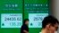 People wearing face masks walk past a bank electronic board showing the Hong Kong share index at Hong Kong Stock Exchange Tuesday, April 14, 2020.