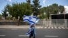 A supporter of Israel's Prime Minister Benjamin Netanyahu waves flags outside his residence in Jerusalem, Sunday, May 24, 2020. Hundreds of protesters calling him the "crime minister" demonstrated outside his official residence, while hundreds of…