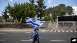 A supporter of Israel's Prime Minister Benjamin Netanyahu waves flags outside his residence in Jerusalem, Sunday, May 24, 2020. Hundreds of protesters calling him the "crime minister" demonstrated outside his official residence, while hundreds of…