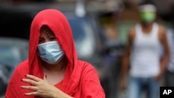A woman wearing a protective mask walks outside a village that was placed under lockdown due to the number of COVID-19 cases among residents in Manila, Philippines on Thursday, March 11, 2021. The Philippine capital placed two villages and two…