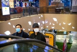 A couple wear face masks as they ride an escalator at a shopping mall in Beijing, March 7, 2020.
