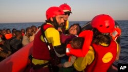 FILE - In this Aug. 20, 2016 file picture a woman from Nigeria and her baby are helped by members of Proactiva Open Arms NGO, before transferring them to an Italian navy ship, during a rescue operation at the Mediterranean sea, about 17 miles north of Sabratah, Libya. 