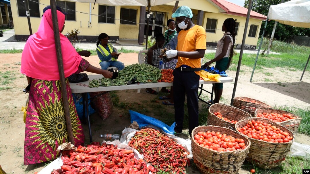 FILE - A vendor wearing a face mask, right, attends to a buyer at a Primary School converted to a makeshift food market for residents of the Ilupeju community in Lagos, Nigeria, April 3, 2020. 