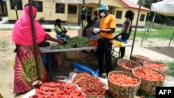 FILE - A vendor wearing a face mask, right, attends to a buyer at a Primary School converted to a makeshift food market for residents of the Ilupeju community in Lagos, Nigeria, April 3, 2020. 