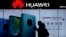 FILE - A woman browses her smartphone as she walks by a Huawei store at a shopping mall in Beijing, Dec. 11, 2018. 