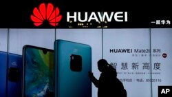 FILE - A woman browses her smartphone as she walks by a Huawei store at a shopping mall in Beijing, Dec. 11, 2018. 