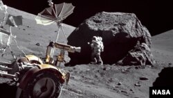Astronaut Harrison Schmitt examines a huge rock on the moon. The Lunar Roving Vehicle is in the foreground.