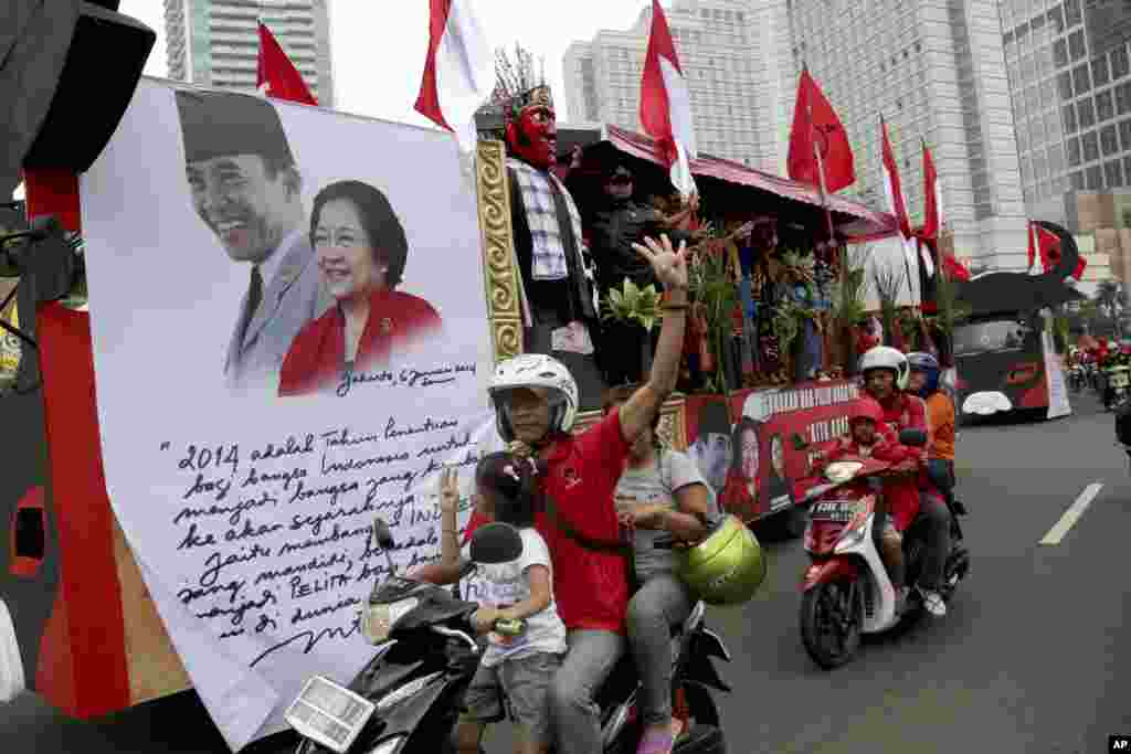 Pendukung Partai Demokrasi Indonesia Perjuangan mengendarai sepeda motor melewati gambar ketua partai Megawati Sukarnoputri dan ayahnya mantan presiden Soekarno, dalam parade yang menyerukan pemilihan damai, Sabtu (15/3). (AP/Tatan Syuflana)