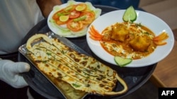 Seorang pelayan membawa makanan 'Kari Covid' dan 'Masker Naan', dua menu bertema virus corona (Covid-19) kepada para pelanggan di restoran mereka di Jodhpur, 3 Agustus 2020. (Foto: AFP)