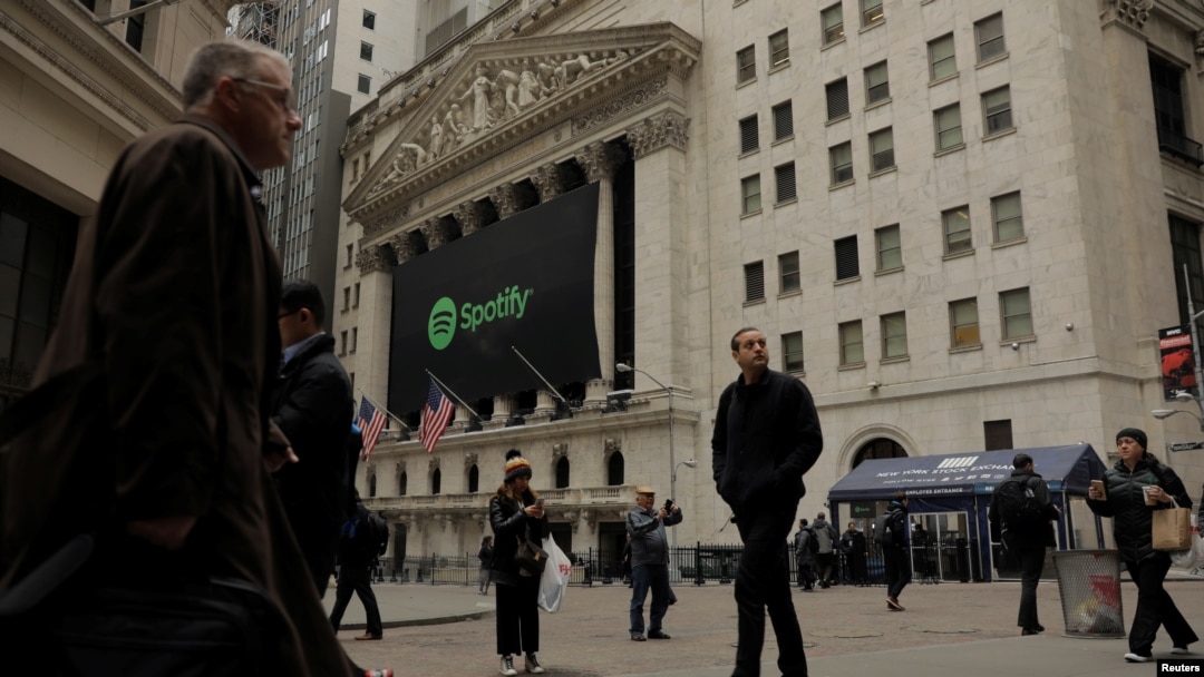 Pedestrians walk past a banner with the Spotify logo on it as the company lists its stock on the New York Stock Exchange with a direct listing in New York, April 3, 2018.