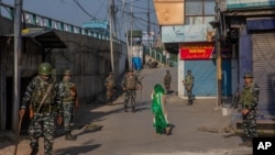 A Kashmiri woman covers her face with a scarf as she walks past paramilitary soldiers standing guard in a closed market area in Srinagar, Indian-controlled Kashmir, Sept. 3, 2021. 