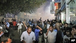 People cover their faces and run as riot police use tear gas to control a clash between anti-government protesters and a group supporting the regime in Male, Maldives, May 3, 2011