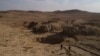 FILE - In this Nov. 11, 2017, photo, two Iraqi men walk near a sinkhole in Khasfa that is believed to contain the remains of people executed by Islamic State militants.