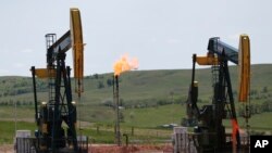 FILE - Oil pumps and natural gas burn off in Watford City, N.D., June 12, 2014.