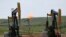 FILE - Oil pumps and natural gas burn off in Watford City, N.D., June 12, 2014.