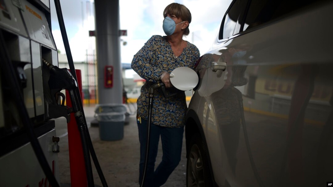 FILE - A woman wears a face mask and gloves at the gas station during a government ordered quarantine aimed at curbing the spread of the new coronavirus in San Juan, Puerto Rico, in March 2020.