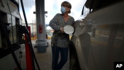 FILE - A woman wears a face mask and gloves at the gas station during a government ordered quarantine aimed at curbing the spread of the new coronavirus in San Juan, Puerto Rico, in March 2020.