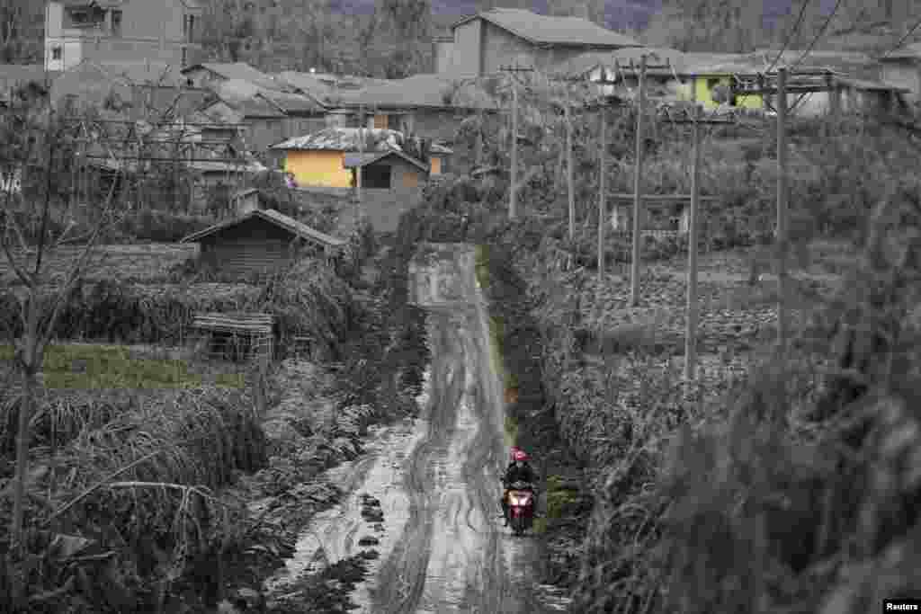 Seorang penduduk desa mengendarai motor di jalan yang tertutup lumpur dari letusan Gunung Sinabung di desa Kuta Rakyat di Karo, Indonesia, 14 Januari 2014.