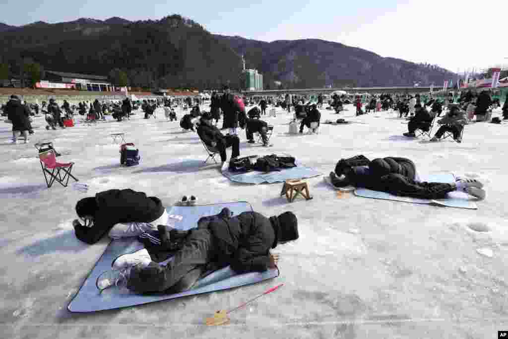 Participants cast lines through holes drilled in the surface of a frozen river during a trout catching contest in Hwacheon, South Korea.