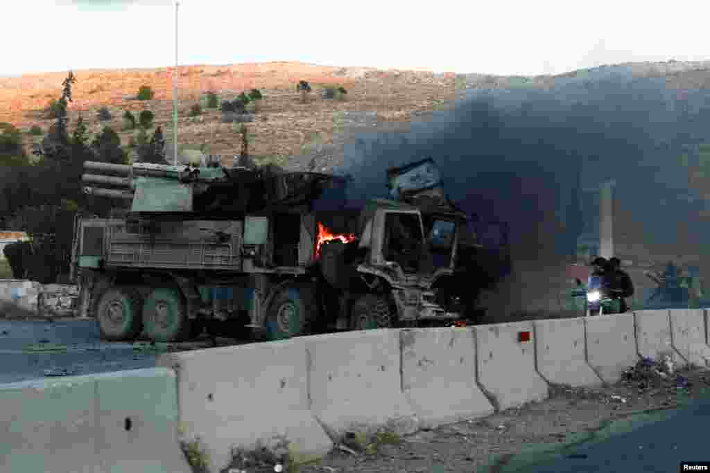 People ride a bike next to a burning military vehicle after Syrian rebels announced that they have ousted Syria&#39;s Bashar al-Assad, in Damascus.