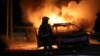 Seorang petugas damkar berdiri di dekat mobil polisi yang terbakar akibat kerusuhan antaretnis di kota Lod, Israel. 