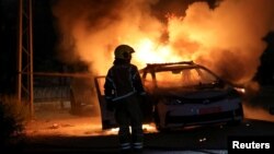 Seorang petugas damkar berdiri di dekat mobil polisi yang terbakar akibat kerusuhan antaretnis di kota Lod, Israel. 