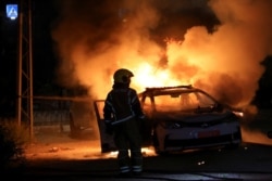 An Israeli firefighter stands near a burning Israeli police car during clashes between Israeli police and members of the country's Arab minority in the Arab-Jewish town of Lod, Israel, May 12, 2021.