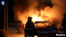 An Israeli firefighter stands near a burning Israeli police car during clashes between Israeli police and members of the country's Arab minority in the Arab-Jewish town of Lod, Israel, May 12, 2021. 