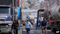 Sejumlah pejalan kaki berjalan melewati rangkaian truk yang memblokade jalan raya di Bogota, Kolombia, sebagai bagian dari aksi protes menentang kenaikan harga solar, pada 3 September 2024. (Foto: AP/Fernando Vergara)