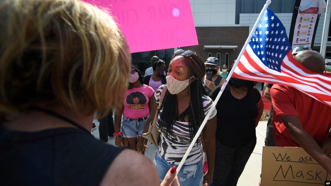 FILE - Pro-mask wearing demonstrator Djenaba Pershay, center, speaks with a non-mask demonstrator, left, at the Cobb County School Board Headquarters during a pro mask wearing protest, in Marietta, Ga., Aug. 12, 2021.