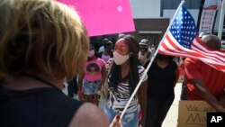 FILE - Pro-mask wearing demonstrator Djenaba Pershay, center, speaks with a non-mask demonstrator, left, at the Cobb County School Board Headquarters during a pro mask wearing protest, in Marietta, Ga., Aug. 12, 2021.