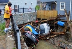 FILE - Residents gather by a bridge to look at cars left crumpled in one of the tributaries of the Patapsco River that burst its banks as it channeled through historic Main Street in Ellicott City, Maryland, May 28, 2018.