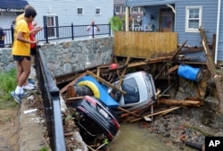 FILE - Residents gather by a bridge to look at cars left crumpled in one of the tributaries of the Patapsco River that burst its banks as it channeled through historic Main Street in Ellicott City, Maryland, May 28, 2018.