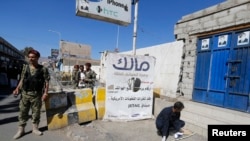 A Houthi militiaman stands guard as a forensic expert inspects the scene of a blast near the republican palace in Sana'a, Feb. 7, 2015.