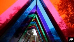 A woman shelters with an umbrella as she walks past an artwork by artist Liz West, part of the Kensington and Chelsea art week, outside the Saatchi Gallery in London.